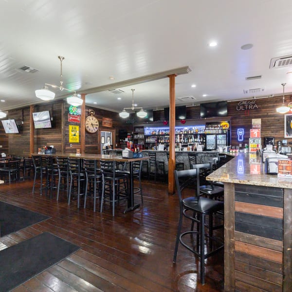 Interior of a bar with wooden walls, dark wood floors, high-top tables, and a fully stocked bar.