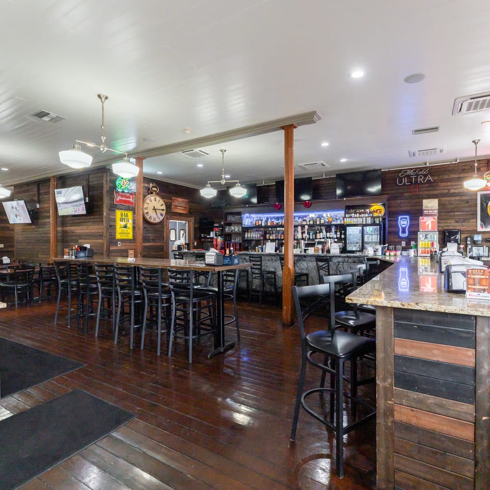 Interior of a bar with wooden walls, dark wood floors, high-top tables, and a fully stocked bar.