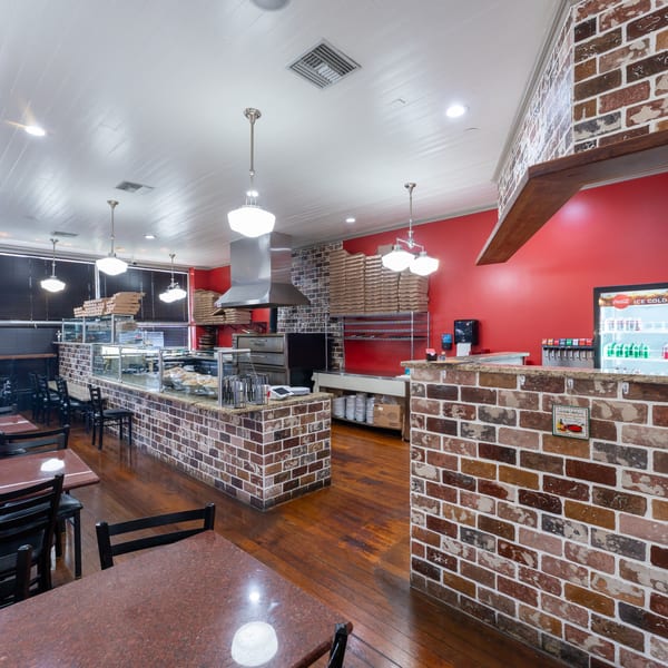 Interior of a pizza restaurant with red walls, brick counters, wooden floors, and dining tables.