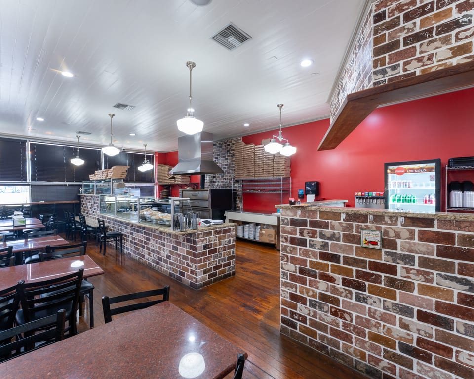 Interior of a pizza restaurant with red walls, brick counters, wooden floors, and dining tables.