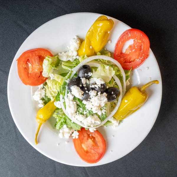 Overhead view of a Greek salad with lettuce, tomatoes, olives, feta, onions, and peppers.