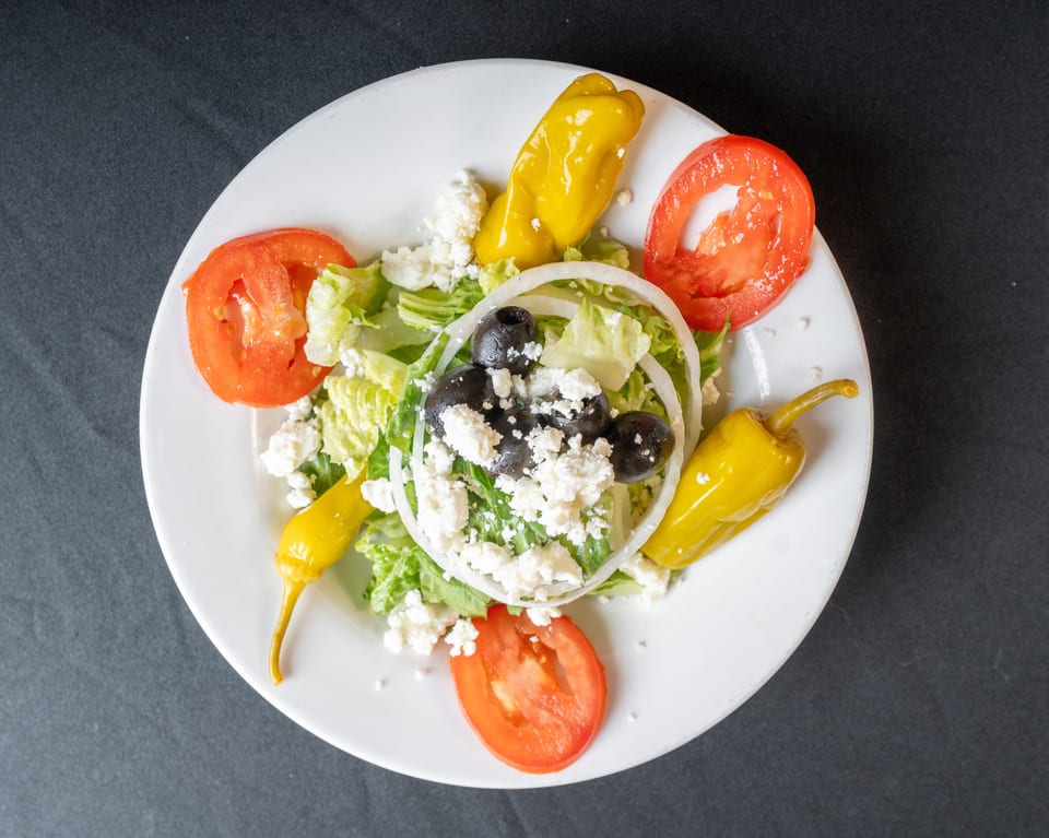 Overhead view of a Greek salad with lettuce, tomatoes, olives, feta, onions, and peppers.