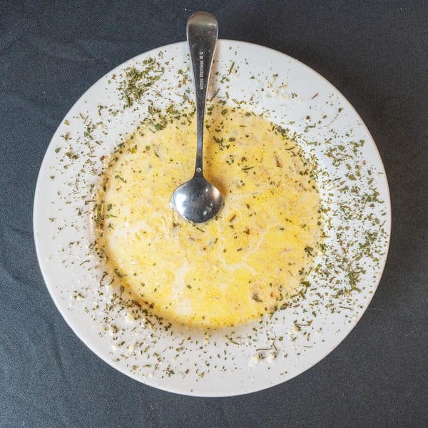 Creamy yellow soup with green herbs and a spoon on a white plate, against a dark background.