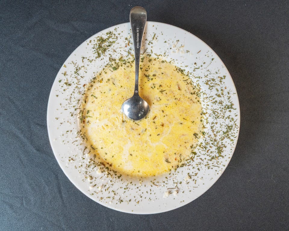 Creamy yellow soup with green herbs and a spoon on a white plate, against a dark background.