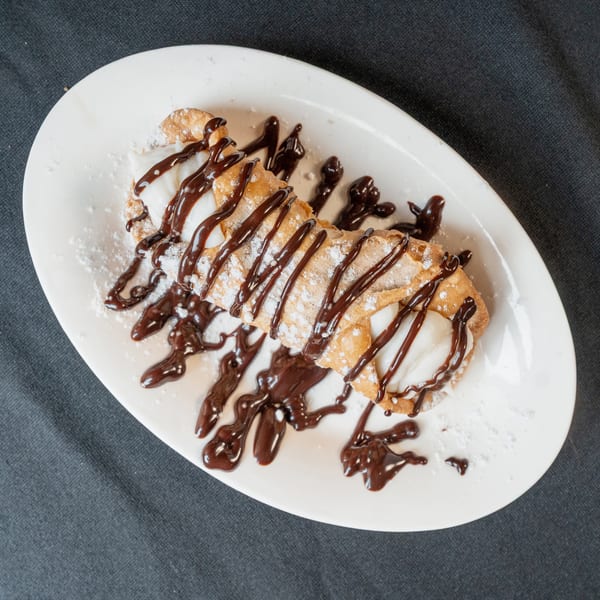 Cannoli dessert drizzled with chocolate sauce and powdered sugar on a white plate.
