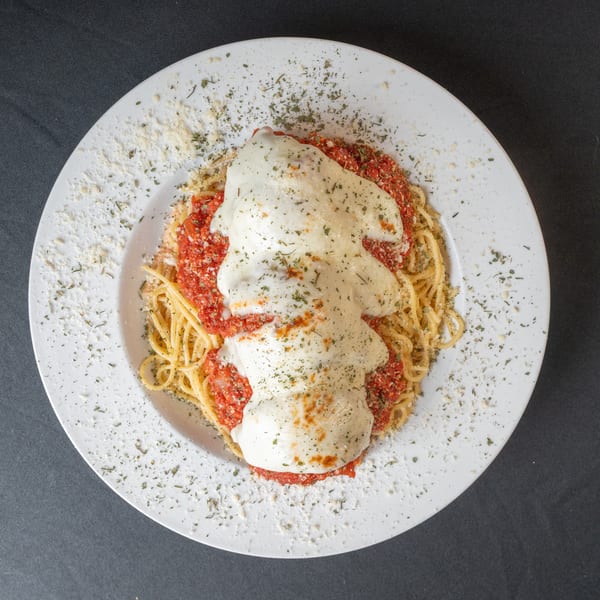 Spaghetti with red sauce and melted mozzarella cheese, topped with herbs and parmesan on a white plate.