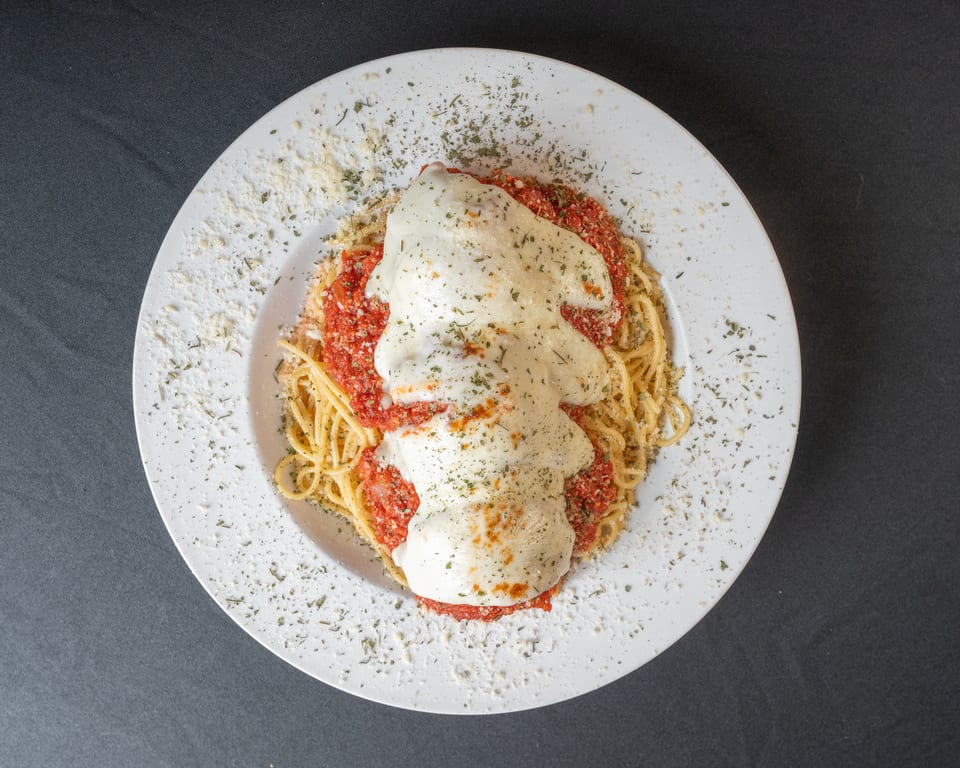 Spaghetti with red sauce and melted mozzarella cheese, topped with herbs and parmesan on a white plate.