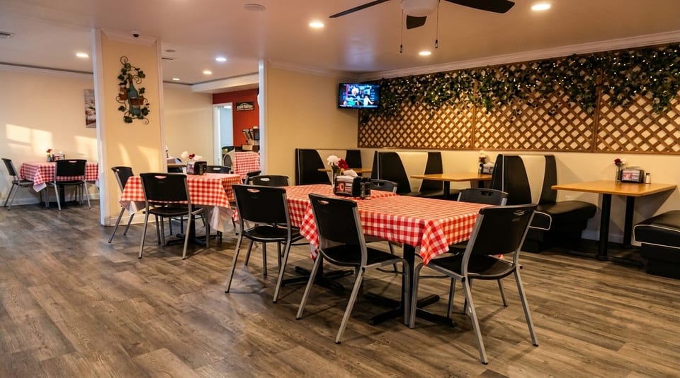 Restaurant interior with red and white checkered tablecloths, black chairs, and booth seating.