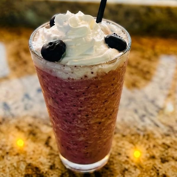 A berry smoothie with whipped cream and blueberries on a speckled countertop.
