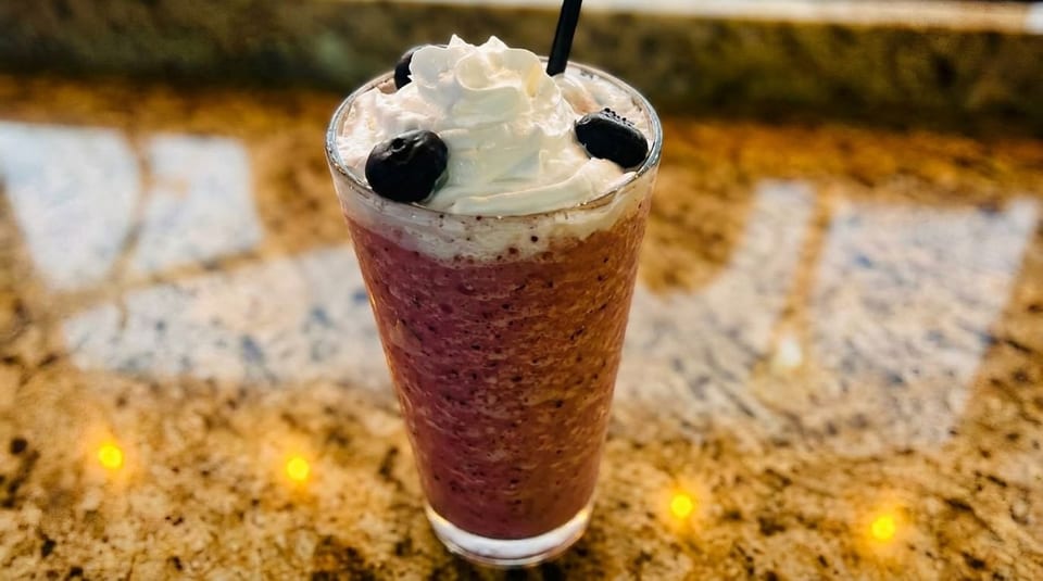A berry smoothie with whipped cream and blueberries on a speckled countertop.
